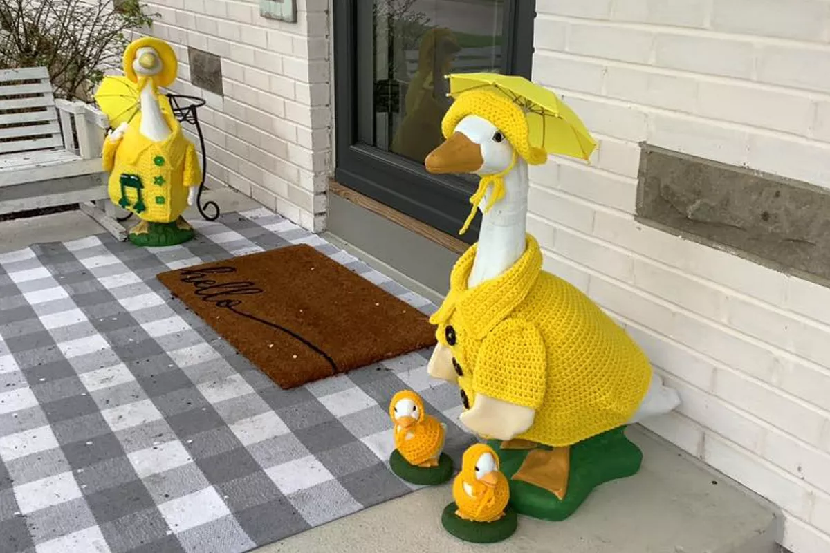 two plastic porch geese in raincoats, flanking a house's front door.