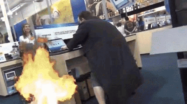 gif of a man in a trenchcoat, miming typing on laptops in a store, with humorous text displayed saying he is hacking the computers