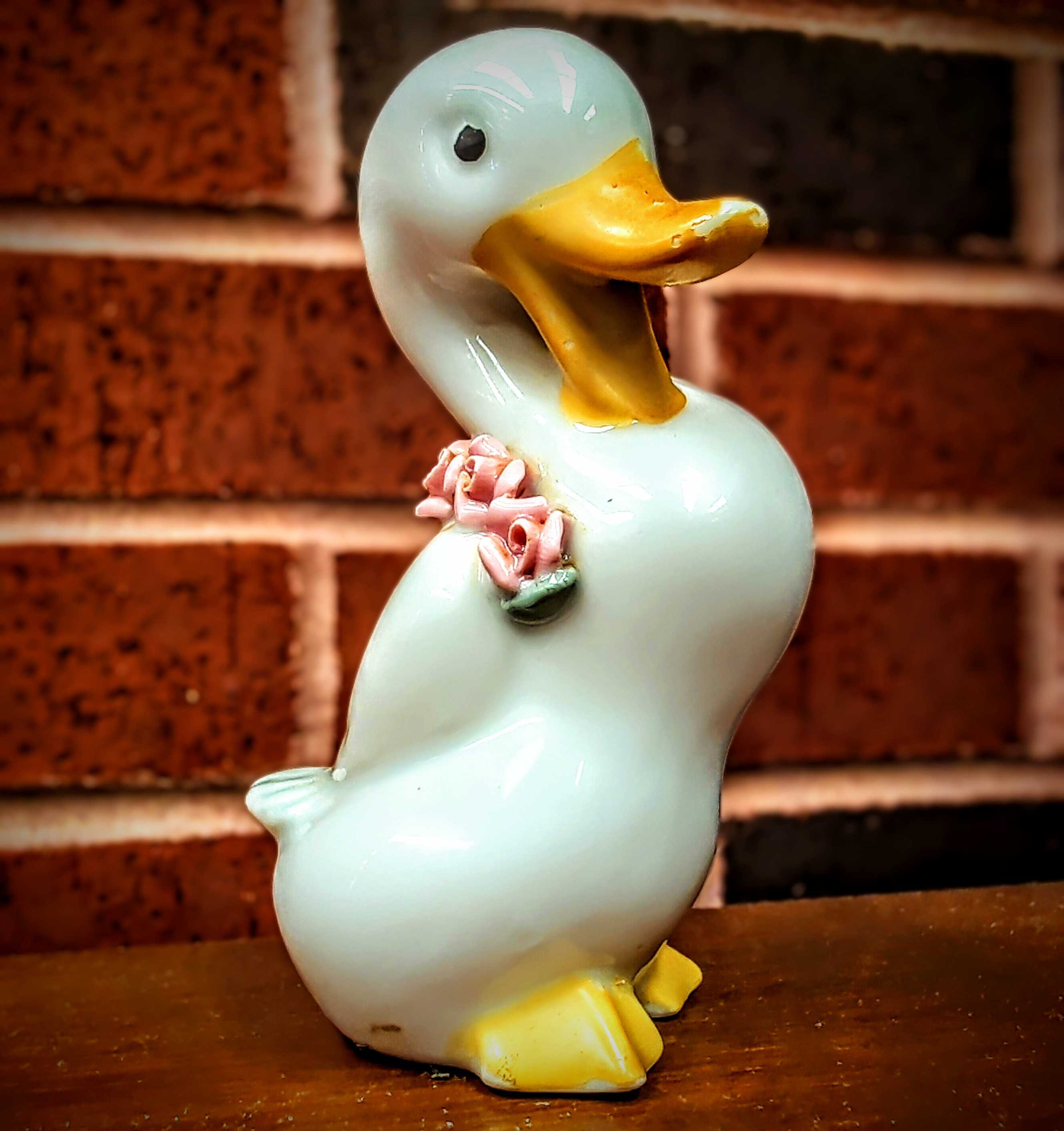 photo of a small goose statuette standing on a wooden table with a brick wall in the background
