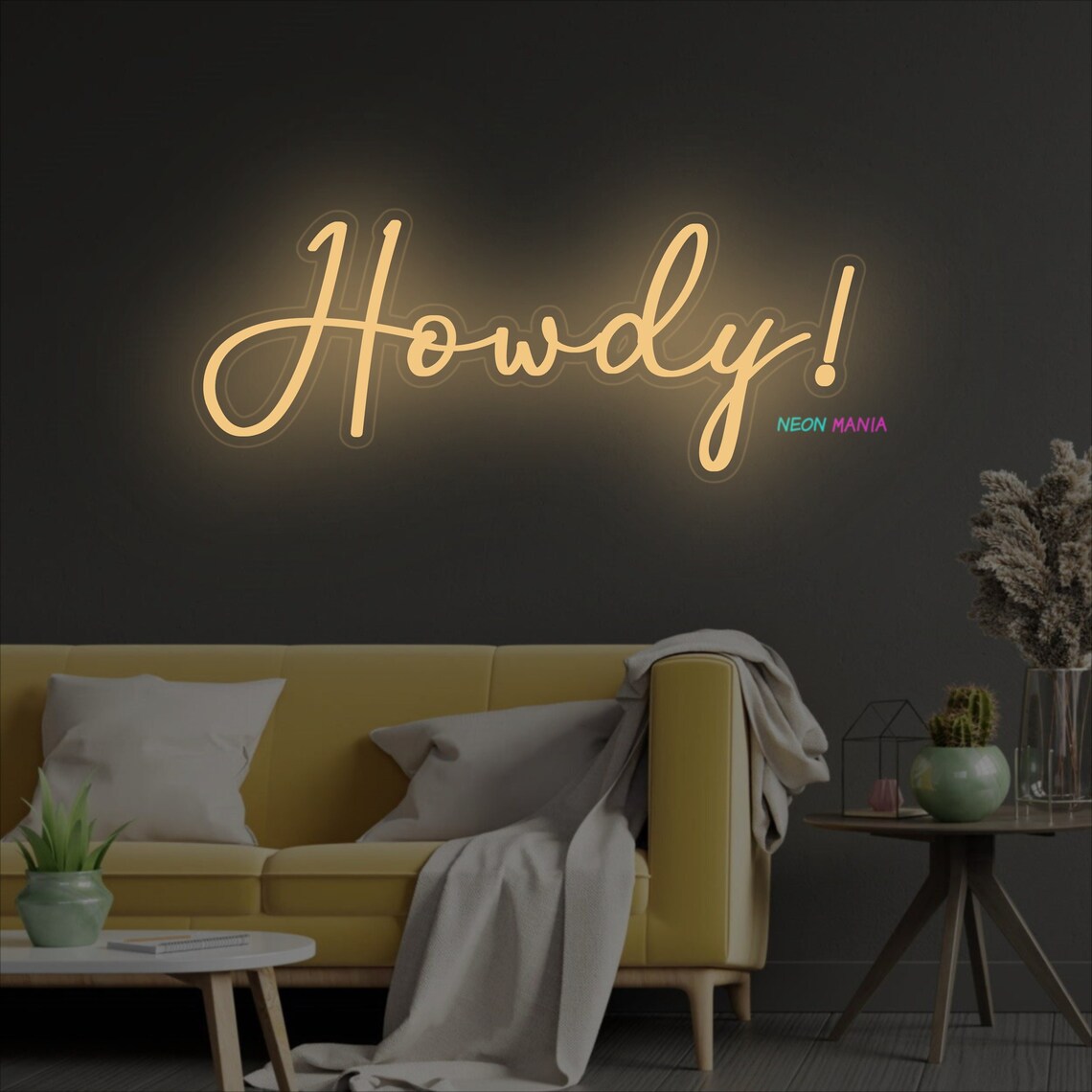 advertising photo of an LED sign that reads howdy exclamation point in cursive, placed on a wall above a couch and table