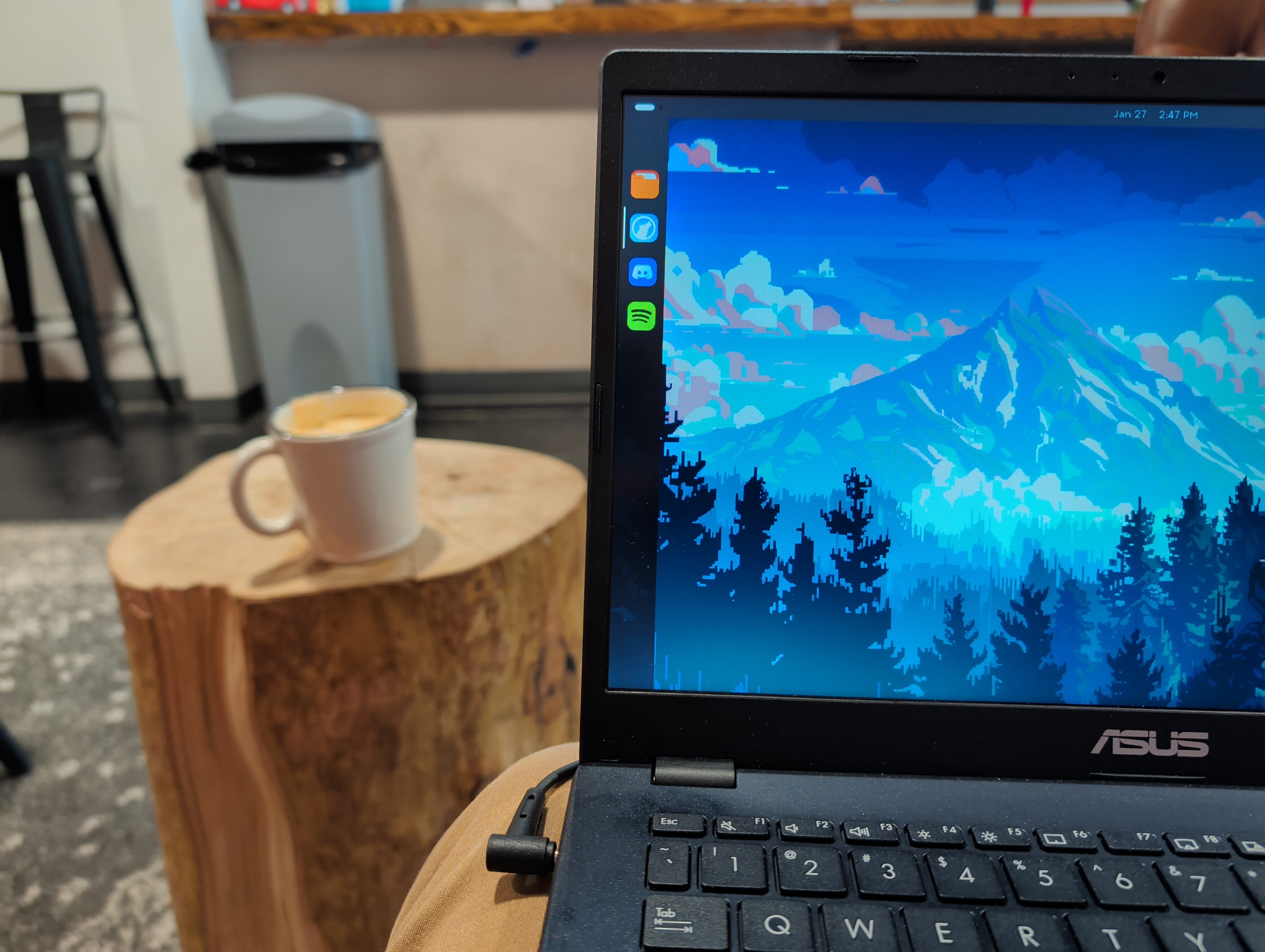 photo of a coffee shop scene, with a corner of a laptop screen and coffee cup in frame.