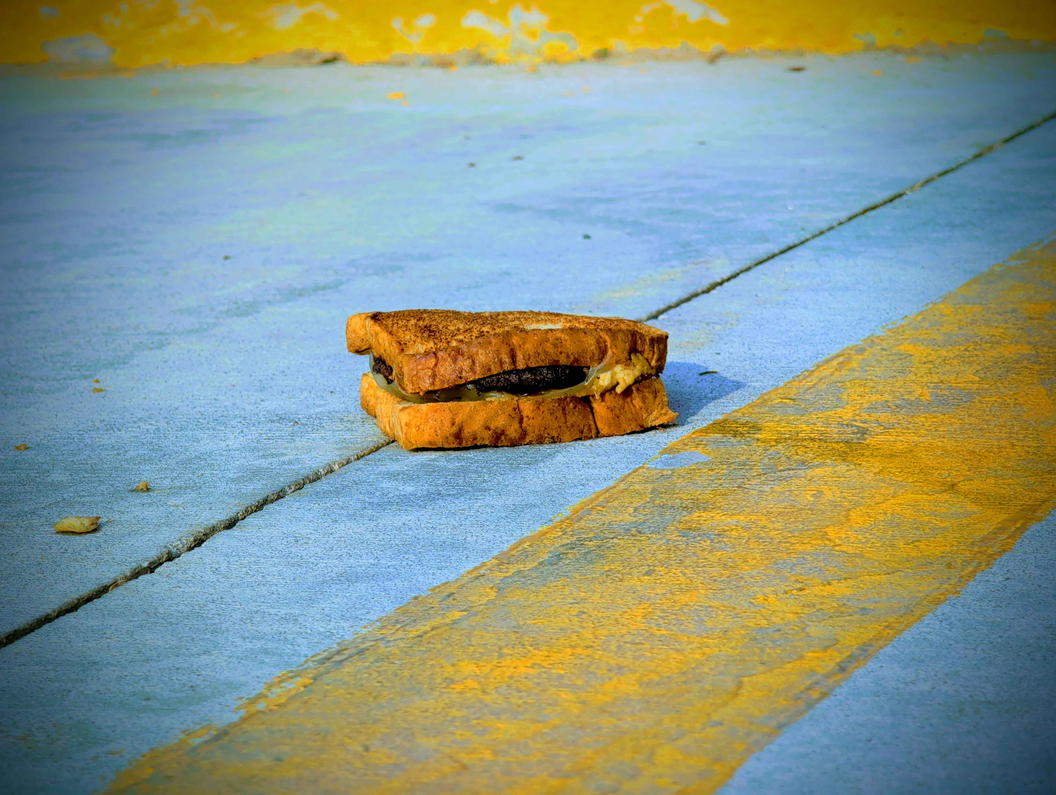 photo of a cheeseburger on toast laying near a yellow line in a parking lot